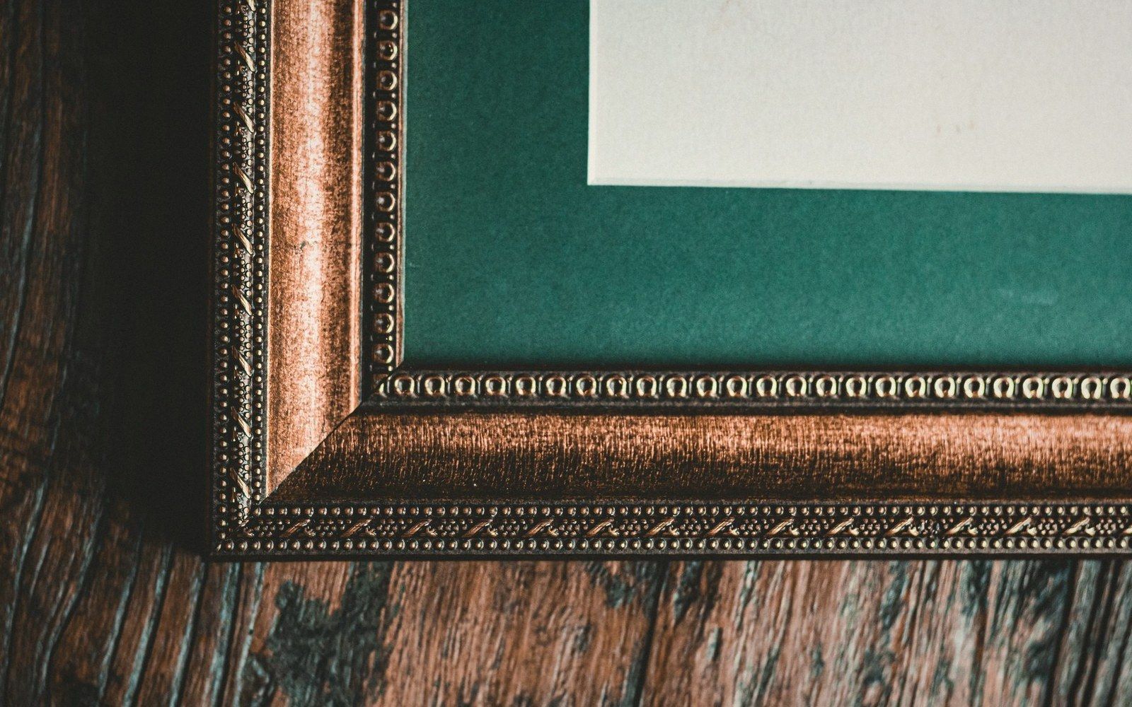 Close-up of a gilded frame corner mitre joint, gold surface slightly worn at the apex, dark background