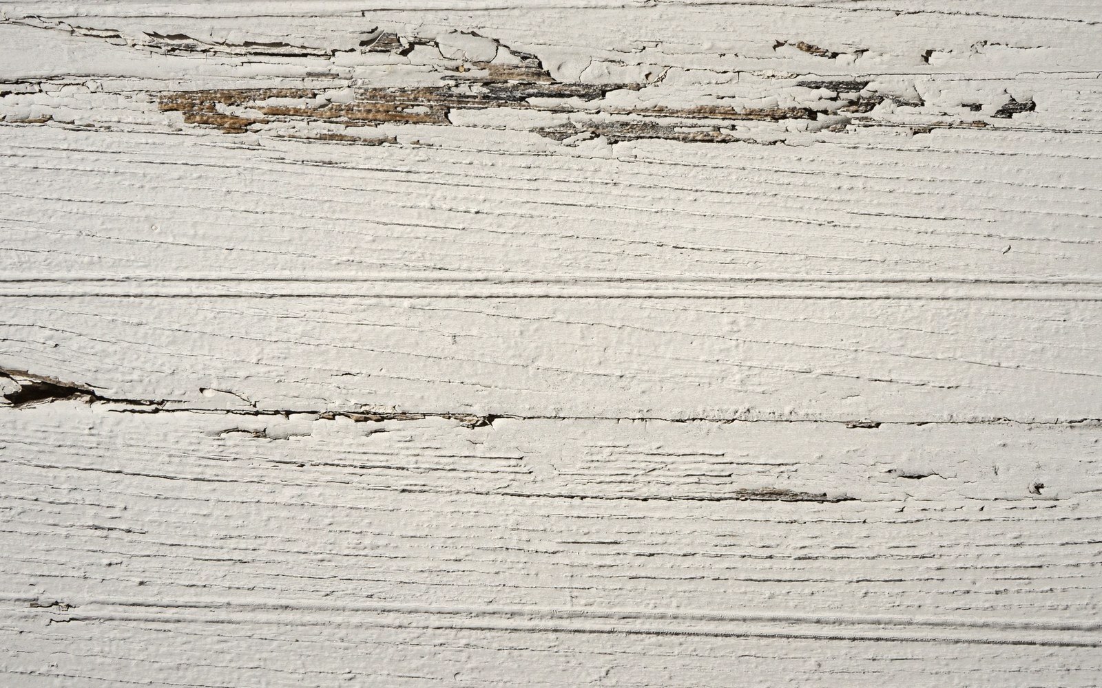 White paint peeling off a wooden plank, revealing bare wood underneath