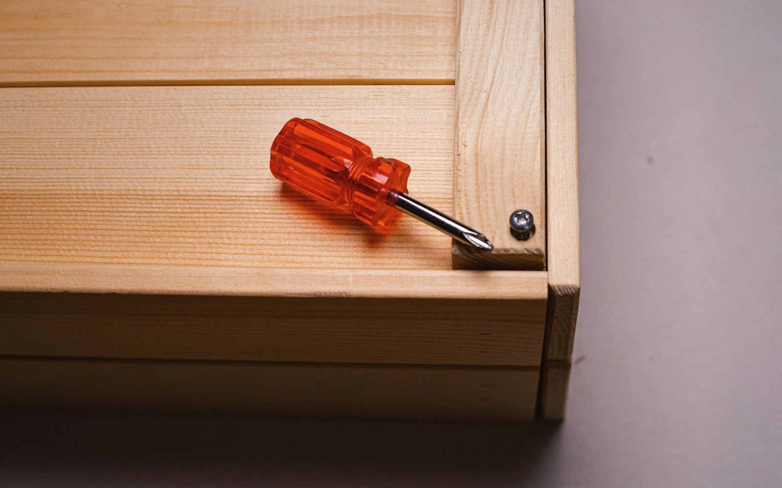 An orange-handled screwdriver resting on a wooden panel near a screw