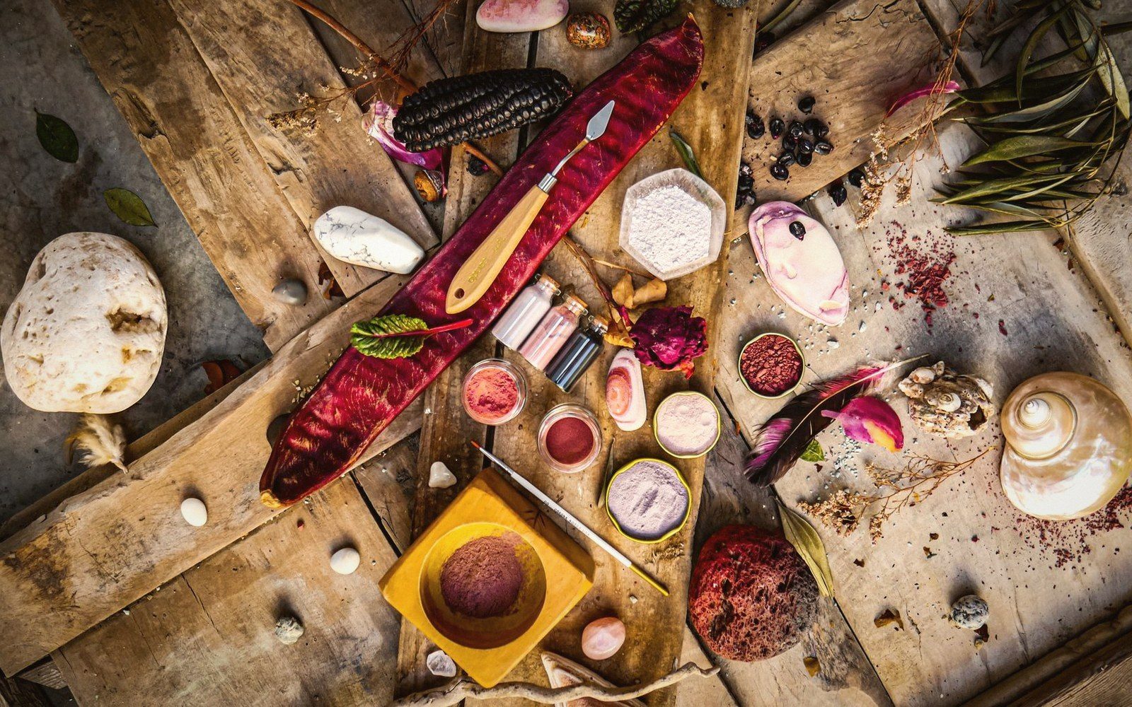 Small jars of colored powders, feathers, dried fruit and a knife arranged on wood