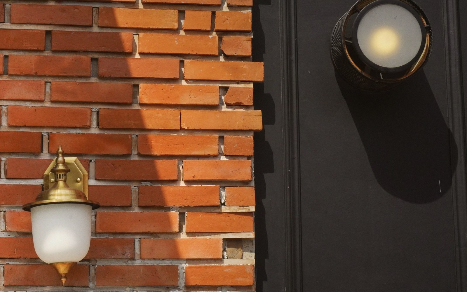 Two brass wall lamps flank a brick wall and dark painted surface, casting long shadows