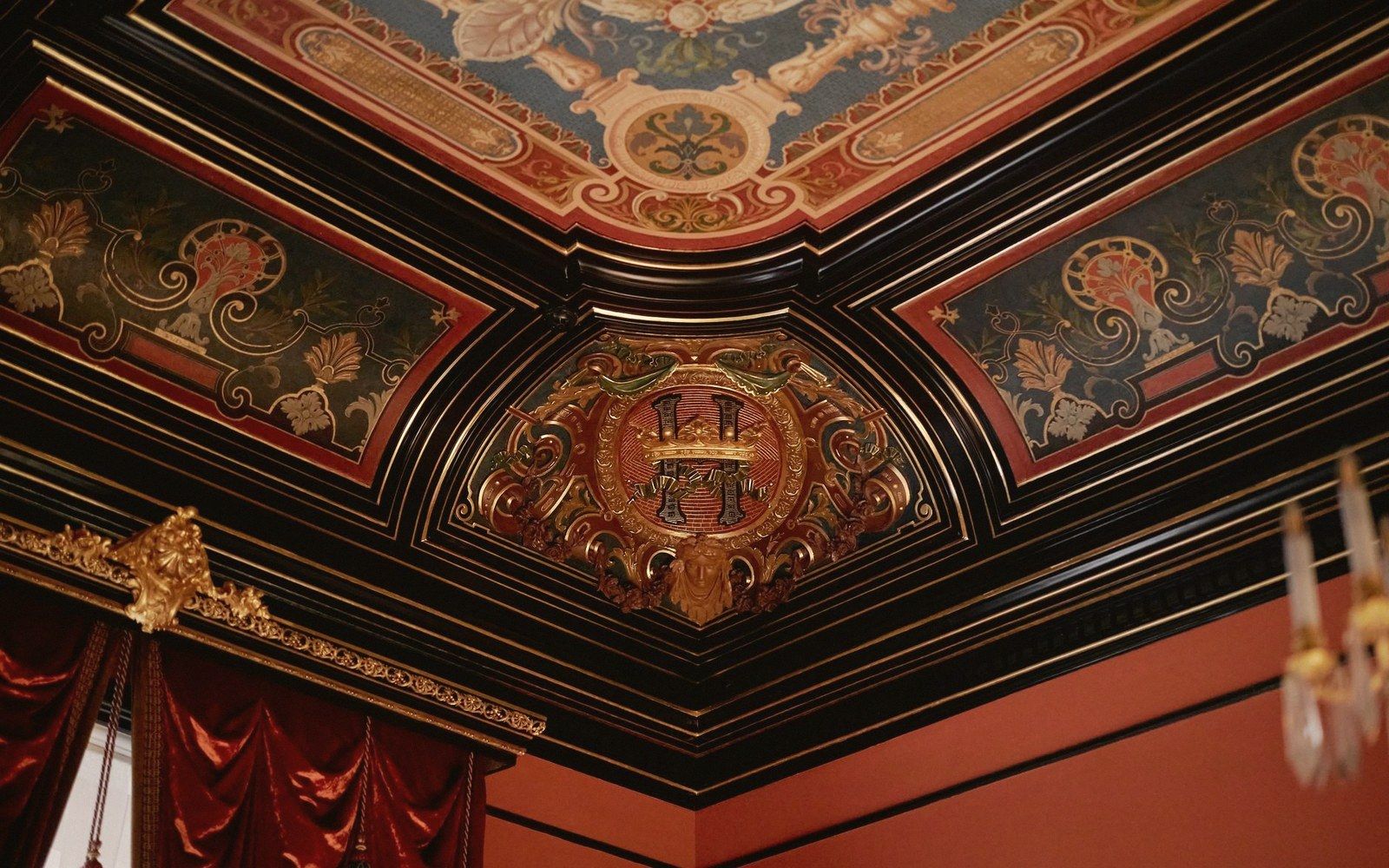 Ornate painted ceiling corner with a crowned monogram medallion and gilded floral panels